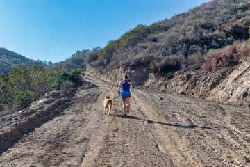 Fototapeta premium Young woman running up a steep dirt hill with her dog 