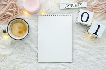 Warm cozy home start new year 1 january on perpetual calendar. Notebook mockup cup of coffee, candle and lights. Flat lay top view - obrazy, fototapety, plakaty