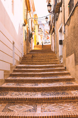 Fototapeta na wymiar Cozy streets and stairs of the old town paved with stone in the form of a pattern. Mediterranean architecture in Spain.