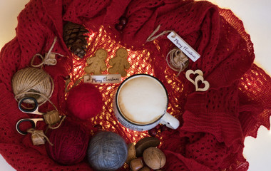 Top view: Craft work tools, colorful balls of wool, cup of cappuccino, happy cookies and festive decorations are on beautiful knitted red scarf. Concept: Merry Christmas holidays and gifts preparation