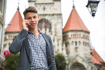 Portrait of the handsome young man who is standing against the background of old gothic build outdoor and speaking by phone