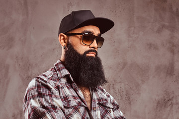 A bearded arabian male wearing checkered shirt sunglasses and cap.