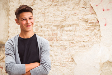 Portrait of the young man who is standing outdoor near the old house wall and smiling