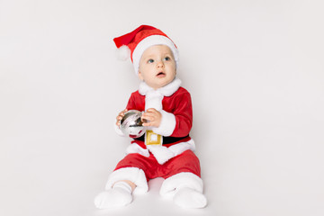 baby girl wearing santa hat on white isolated background holding in her hands Christmas ball