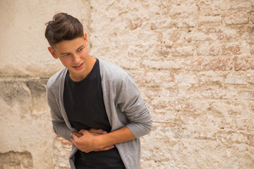 Fototapeta premium Portrait of the young man who is standing outdoor near the old house wall and having the stomach ache