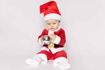 baby girl wearing santa hat on white isolated background holding in her hands Christmas ball