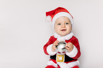 baby girl wearing santa hat on white isolated background holding in her hands Christmas ball