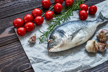 Raw dorado fish with garlic and tomatoes on rustic background. Sea bream or dorada fish. Top view, copy space