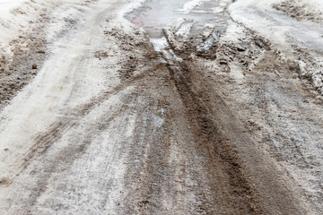 Winter puddles and snow slush on road with traces of tires during the thaw