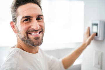 A Cheerful man set the thermostat at house