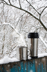 Iron mugs of hot drink on a snow covered terrace.