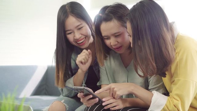 Asian women using smartphone checking social media in living room at home, group of roommate friend enjoy funny moment while lying on the sofa. Lifestyle women relax at home concept.