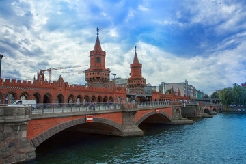 Fototapeta na wymiar Beautiful red brick bridge. Towers with decorations and weathercocks. Cityscape with river and original architecture.