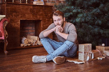 A young handsome man looking at a camera while sitting on a floor surrounded by gifts