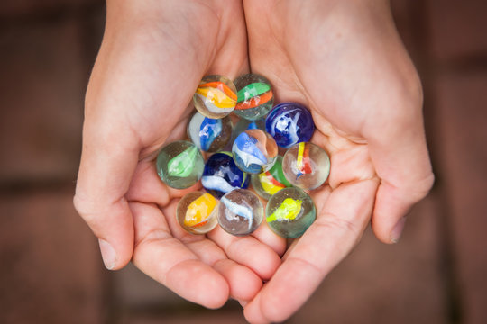 Colorful game marbles in the hands of a child, top view