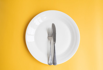 High angle view of knife and fork on white dinner plate against yellow background