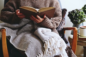 Cozy home with chair and cushions, book and blanket. Hygge life, home interior. Girl reading book