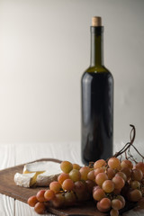 Obraz premium Bottles of wine on a white wooden background with grapes and Camembert cheese