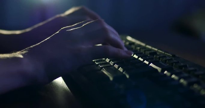 Typing on keyboard at night. Dark background lighting. Close-up