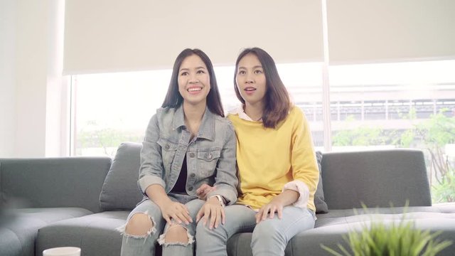 Lesbian Asian couple watching TV laugh in living room at home, sweet couple enjoy funny moment while lying on the sofa when relax at home. Lifestyle couple relax at home concept.