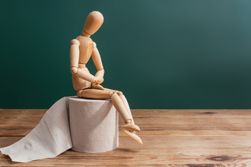 Wooden figure sit on a roll of toilet paper. Concept of the problem with digestion. - obrazy, fototapety, plakaty