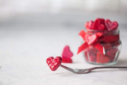 Valentine's day concept. jar with small hearts red and pink on a light background. heart on a fork.selective focus