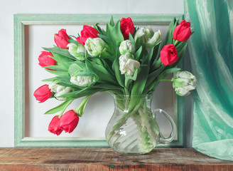 Classic still life with red and white tulips on the background of green empty picture frame and greed drapery