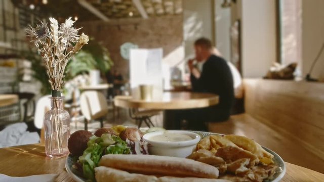 Blurred cafe background with people eating and plate of falafel on foreground