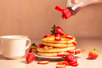 MANO DE MUJER SIRVIENDO JARABE SOBRE PANCAKES CON FRESA
