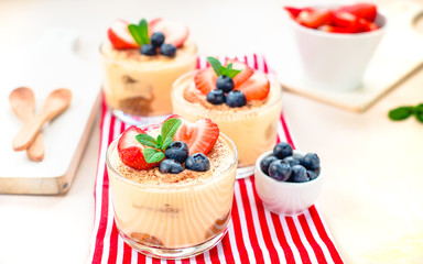 homemade, exquisite dessert tiramisu in glasses decorated with strawberry, blueberry, mint on white wooden table