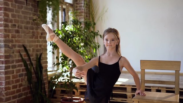 Charming girl in black tutu performs element of classical ballet exercise at the ballroom. A young beautiful ballerina in black tutu doing stretching and warm-up exercises