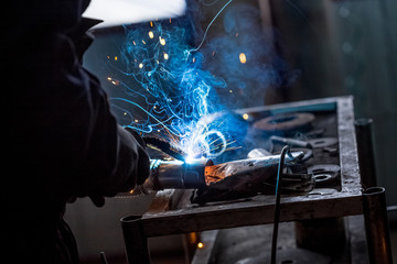 Male worker wearing protective gloves while repairing car exhaust pipe with welding machine