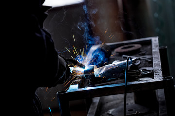 Male worker wearing protective gloves while repairing car exhaust pipe with welding machine
