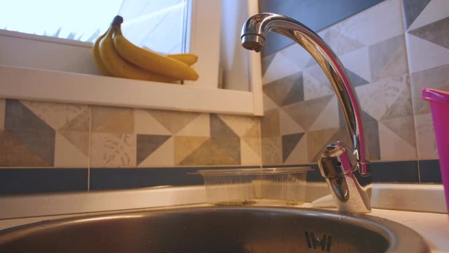 Water drop drips from tap and falls into kitchen sink