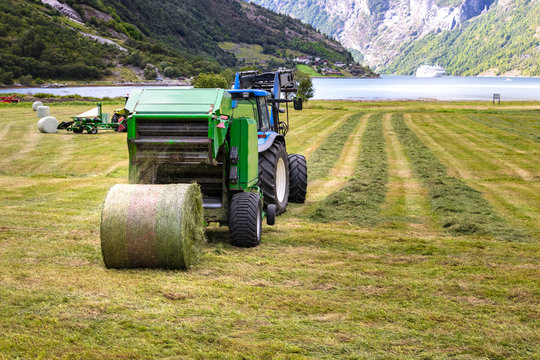 Small tractor with round baler unloading on a field in Geiranger, Norway.