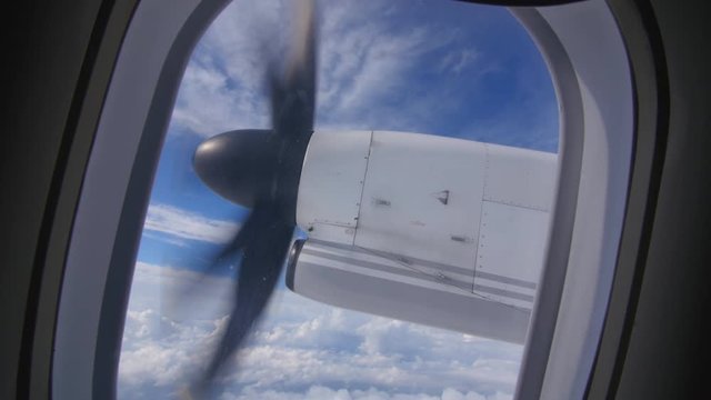 Turboprop propellor engine viewed through window of passenger airplane. Fluffy clouds.