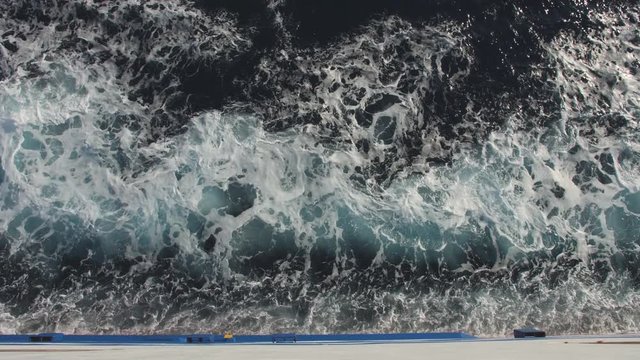 White bow waves go fast by the side board of a big ferryboat. Cruising the sea
