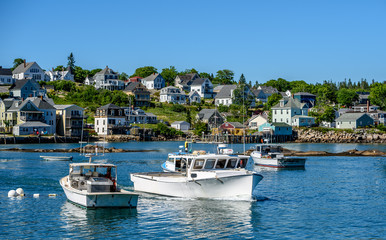 Fototapeta na wymiar Maine Lobster Boats Anchored in the Bay in Front of a Quaint New England Village