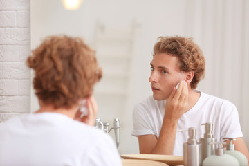 Young man applying shaving foam near mirror at home