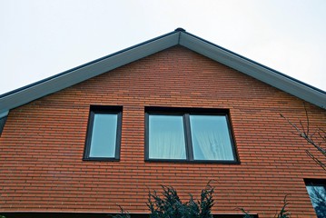 windows on brown brick attic wall against the sky