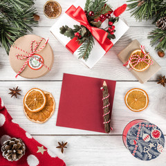 Creative layout frame made of Christmas tree branches, paper card note, pine cones, gifts, Christmas sweater on white wooden background. Xmas and New Year theme. Flat lay, top view