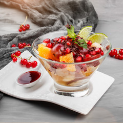 Fruit salad with banana, orange, grapes and pomegranate in glass bowl on grey background. Healthy breakfast