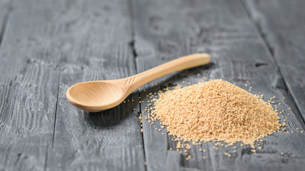 A pile of amaranth seeds and a wooden spoon on a dark wooden table.