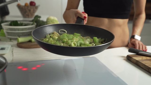 Closeup cooking fried green onions and celery tosses them in hot frying pan. Slow motion
