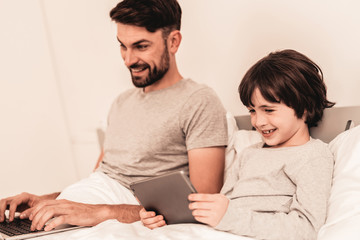 Son with Father Using Laptop in Bed in Morning.