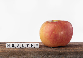 Red apple on a wood shelf and letters spelling out the word "HEALTHY" next to it.