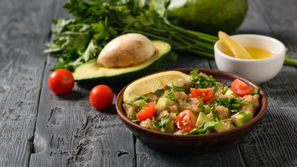 Salad of amaranth, avocado, pepper, lemon and parsley seeds with olive oil on a black table.