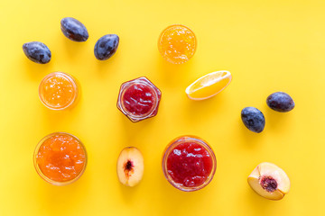 Jams different tastes made of fruits and berries near pieces of fruits on yellow background top view