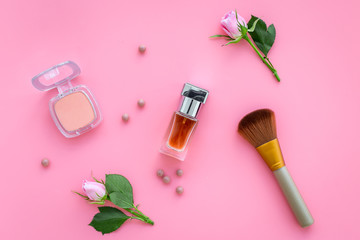Obraz na płótnie Canvas Rose tone cosmetics. Bulk, eyeshadow, perfume among rose flowers on pink background top view
