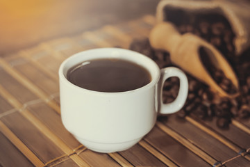cup of black coffee and grains of coffee in a bag on a wooden table